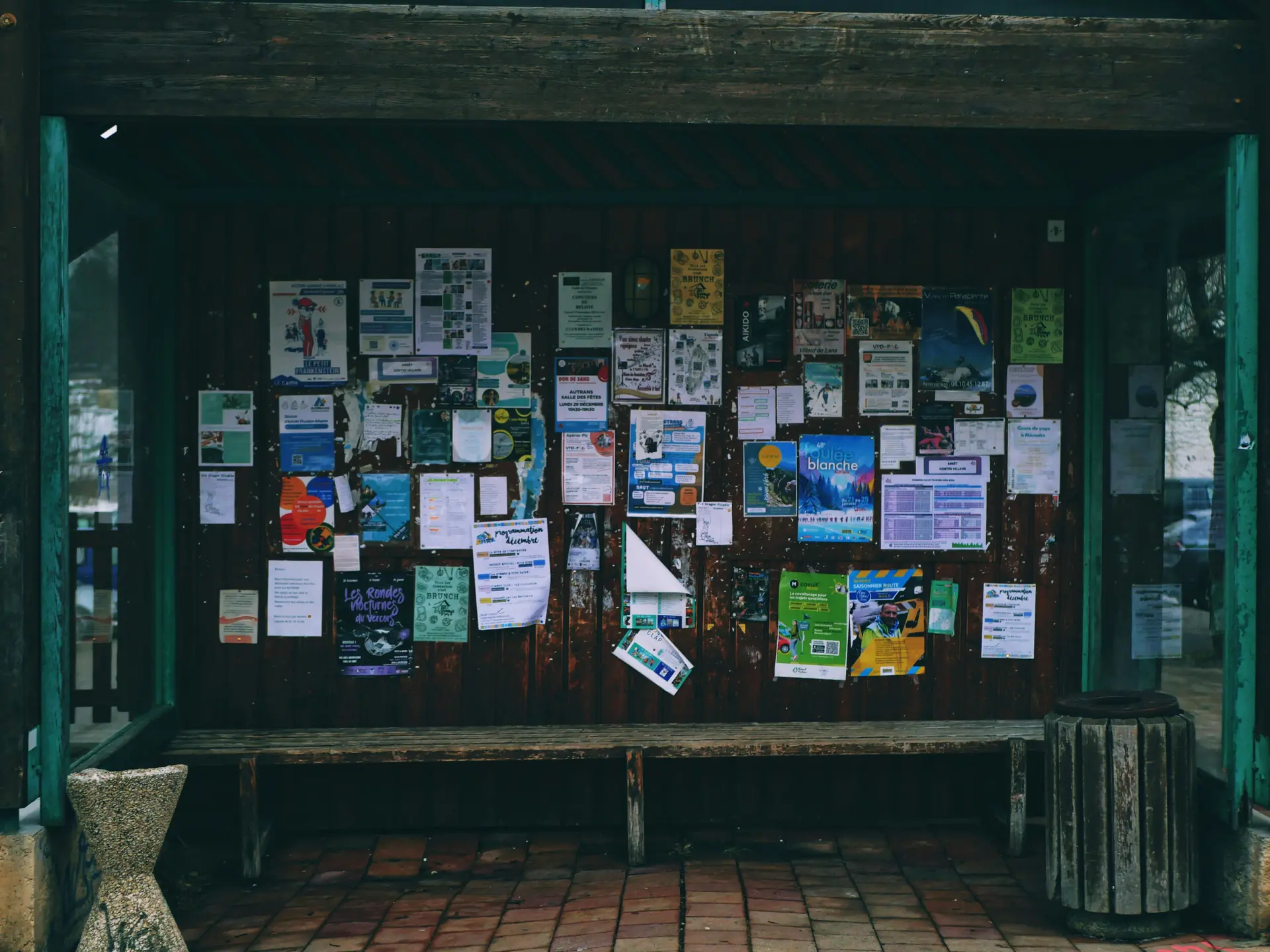 A crowded wooden community bulletin board covered in overlapping local flyers and notices